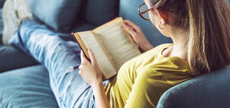 Une jeune femme assise sur son canapé en train de lire